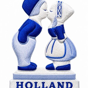 Peut inclure: Un écusson brodé représentant deux personnages en tenue traditionnelle néerlandaise qui s'embrassent, debout sur une base rectangulaire avec le mot HOLLAND brodé en lettres capitales bleues. Le motif utilise des fils bleus et blancs.