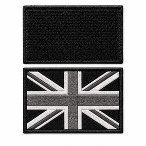 May include: Two rectangular embroidered patches. The top patch is solid black with a stitched border. The bottom patch features a monochrome Union Jack flag design in shades of black, gray, and white, also with a stitched border.