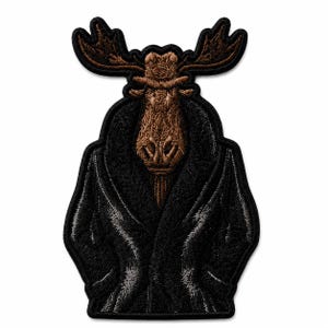 May include: An embroidered patch featuring a brown moose head with large antlers, wearing a black coat with a textured finish. The design is outlined in black thread, creating a distinct silhouette of a moose dressed in formal outerwear.