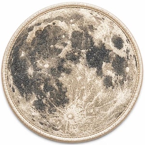 May include: A circular embroidered patch featuring a detailed lunar surface design. The moon is rendered in shades of cream, beige, gray, and charcoal thread, showcasing craters and textured terrain with a thick, stitched tan border edge.
