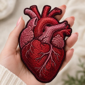 May include: An embroidered patch shaped like an anatomical human heart. The design features intricate thread work in various shades of deep red, crimson, and burgundy, highlighting the arteries and veins with detailed stitching and a dark border.