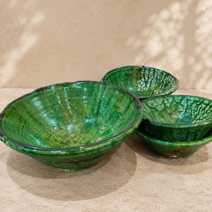 Puede incluir: Un juego de tres cuencos de cerámica encajables con un esmalte verde esmeralda brillante y vibrante. Los cuencos tienen una superficie orgánica y texturizada con crestas visibles y un borde ligeramente irregular hecho a mano.