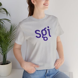 Op de afbeelding: Een lichtgrijs t-shirt met korte mouwen en de paarse tekst sgi in het midden op de borst gedrukt. Het shirt heeft een ronde hals en een standaard pasvorm, wat zorgt voor een strakke en eenvoudige uitstraling voor dagelijks gebruik.