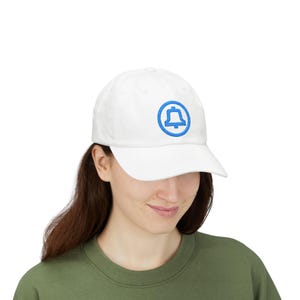May include: White baseball cap with a blue bell logo. The cap has a curved brim and a classic six-panel design. The bell logo is embroidered on the front of the cap. The cap is made of a soft, breathable fabric.