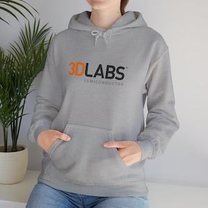 Puede incluir: Sudadera con capucha gris con el texto "3D LABS SEMICONDUCTOR" en naranja y negro. La sudadera tiene un bolsillo delantero y una capucha con cordón. La persona lleva vaqueros azules.