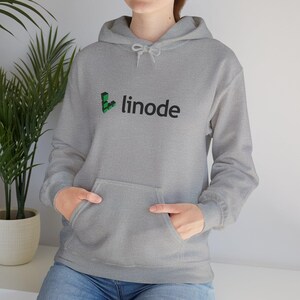 Könnte beinhalten: Ein graumelierter Kapuzenpullover mit einer Kängurutasche auf der Vorderseite und langen Ärmeln. Auf der Brust befindet sich ein grünes geometrisches Logo, gefolgt von dem schwarzen Schriftzug linode. Der Hoodie hat eine passende graue Kordel.