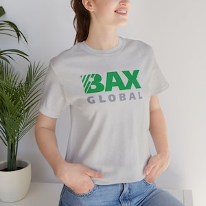May include: A light grey crew neck t-shirt featuring the green text "BAX" above the grey text "GLOBAL". The shirt is made of a soft material. The t-shirt is being worn by a person.