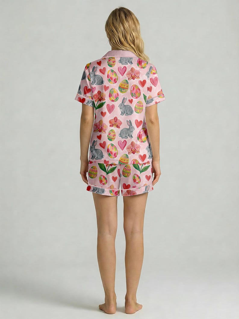 Puede incluir: Conjunto de pijama rosa con tem&aacute;tica de Pascua, con una camisa de manga corta y pantalones cortos a juego. El conjunto est&aacute; adornado con un patr&oacute;n repetido de huevos de Pascua, conejos grises, corazones rosas y flores. Los pijamas son de tela suave y ligera.