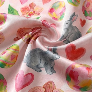 Puede incluir: Una tela rosa con un patr&oacute;n repetido de huevos de Pascua, conejos grises, corazones rosas y elementos florales. El dise&ntilde;o de acuarela presenta colores pastel y una textura suave y fluida, ideal para proyectos de primavera.