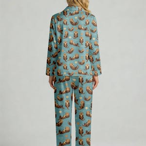 May include: A two-piece pajama set featuring a teal background with a repeating pattern of brown otters, seashells, and waves. The long-sleeved top has a collared neckline and button closure. The matching pants have a straight leg design.