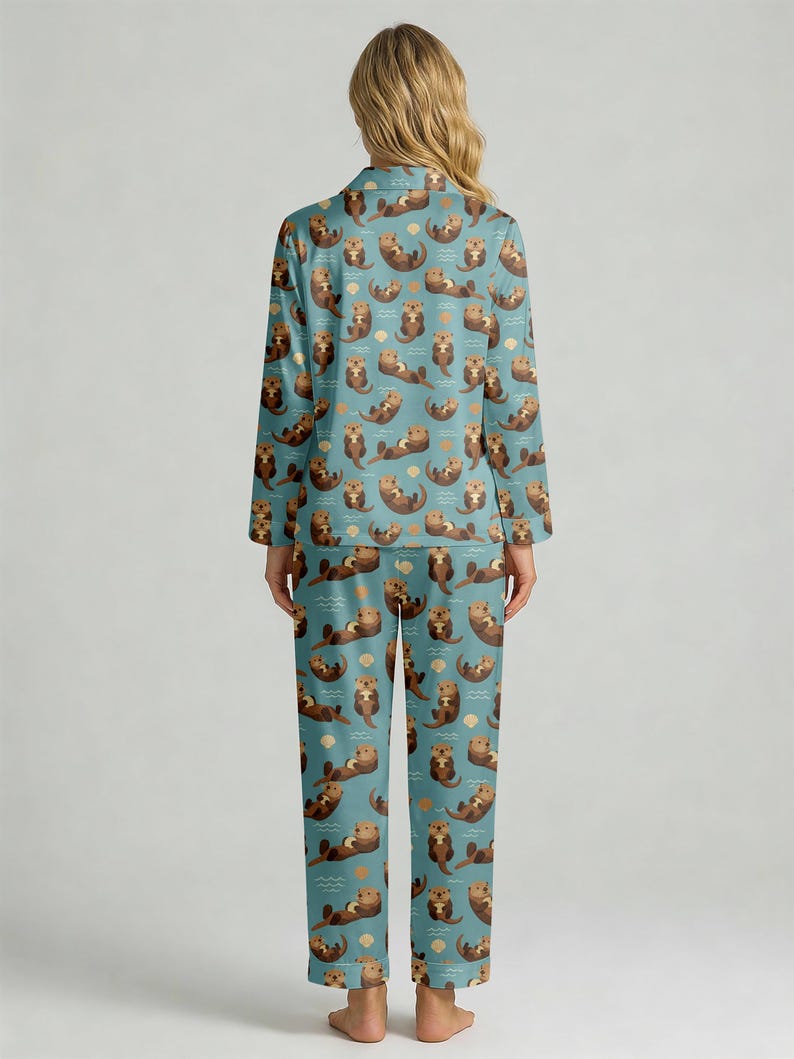 May include: A two-piece pajama set featuring a teal background with a repeating pattern of brown otters, seashells, and waves. The long-sleeved top has a collared neckline and button closure. The matching pants have a straight leg design.