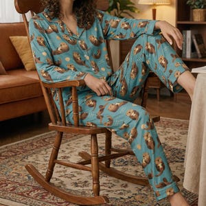 May include: Teal pajama set featuring a repeating pattern of otters and seashells. The long-sleeved top has a collared neckline and button closure. The matching pants have an elastic waistband. The pajamas are made of a soft, comfortable material.