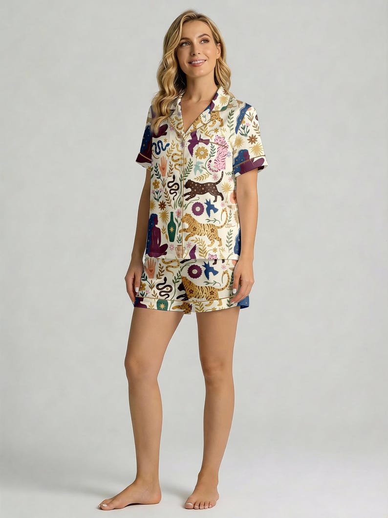 Pode incluir: Um conjunto de pijama de duas pe&ccedil;as creme. A parte de cima e os cal&ccedil;&otilde;es s&atilde;o adornados com um padr&atilde;o colorido de tigres, cobras e elementos florais. A parte de cima tem mangas curtas com acabamento roxo escuro, e os cal&ccedil;&otilde;es t&ecirc;m acabamento azul.