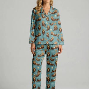 May include: A teal pajama set featuring a repeating pattern of brown otters, waves, and seashells. The long-sleeved top has a button-down front and notched collar. The matching pants have a relaxed fit. The pajamas are made of a soft, silky material.