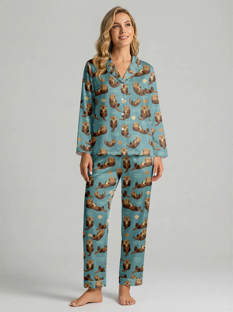 May include: A teal pajama set featuring a repeating pattern of brown otters, waves, and seashells. The long-sleeved top has a button-down front and notched collar. The matching pants have a relaxed fit. The pajamas are made of a soft, silky material.