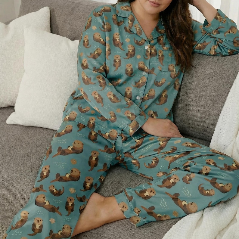 May include: Teal pajama set featuring a repeating pattern of brown otters. The long-sleeved top has a button-down front and a notched collar. The matching pants have an elastic waistband. The pajamas are made of a soft, silky material.