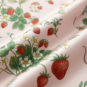 Puede incluir: Primer plano de una tela rosa con un patr&oacute;n repetido de fresas, flores blancas, hojas verdes y peque&ntilde;os hongos. La tela tambi&eacute;n presenta ilustraciones de ratones azules y grises.