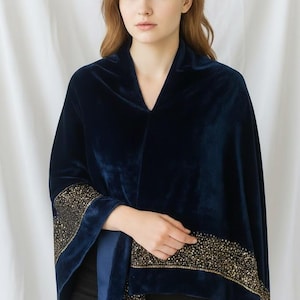 May include: A navy blue velvet cape with gold beaded trim. The cape has a V-neck and wide sleeves. The gold beading is concentrated on the sleeve edges and along the bottom hem. The cape is worn over black clothing.