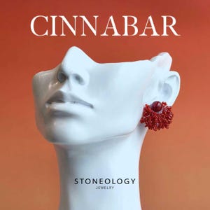 Puede incluir: Un busto blanco con un pendiente rojo y blanco. El pendiente es un grupo de cuentas rojas alrededor de una piedra roja. La palabra "CINNABAR" está en la parte superior y "STONEOLOGY JEWELRY" en la inferior, sobre un fondo naranja.