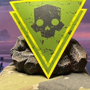 May include: A green and yellow triangular sticker with a black skull and crossbones design. The sticker has a distressed, worn look.