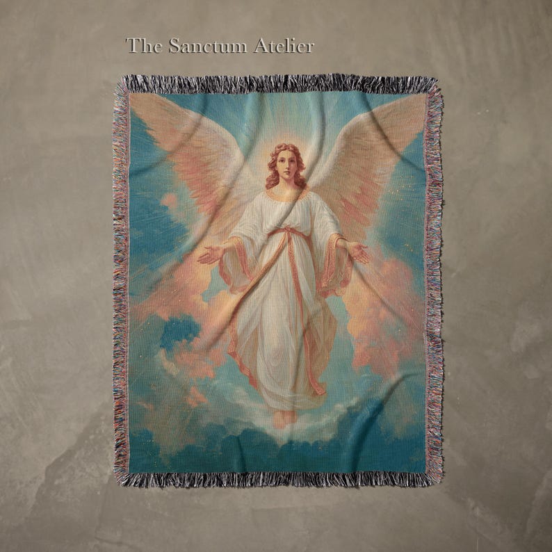 May include: A woven throw blanket featuring a celestial image of an angel with large wings, dressed in white robes, against a backdrop of clouds and a blue sky. The text "The Sanctum Atelier" is at the top. The blanket has a fringed edge.
