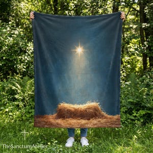 Könnte beinhalten: Eine rechteckige Wohndecke mit dunkelblauem Hintergrund und einem hell leuchtenden Stern in der oberen Mitte, der Licht auf einen Haufen goldbraunes Stroh am unteren Rand wirft. Das Motiv zeigt eine Krippenszene mit einem Stern.