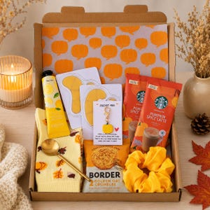 May include: A gift box containing a yellow pair of socks with autumn leaves, a gold spoon, a yellow tube of hand cream, two eye masks, a pumpkin-shaped keychain with a card reading Pocket Hug, a pack of Border oat crumbles, and a yellow scrunchie.