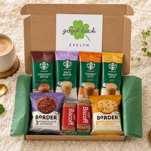 May include: A cardboard gift box containing four Starbucks instant coffee packets in Chocolate Mocha, White Mocha, Caramel Latte, and Vanilla Latte, two Biscoff biscuit packs, and two Border cookie packs, with a card reading good luck EVELYN.