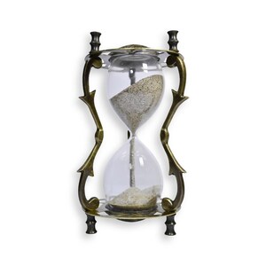 May include: An hourglass with a clear glass bulb filled with sand, set in an ornate brass-colored metal frame. The hourglass is designed with decorative curves and a circular base, showcasing a vintage aesthetic. The sand is a light tan color.