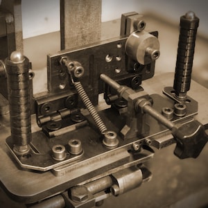 Può includere: Primo piano di una macchina metallica vintage con vari componenti meccanici. La macchina, in tonalità seppia, presenta una serie di leve, molle e parti cilindriche. Il design suggerisce uno strumento o un'attrezzatura di un'epoca precedente.