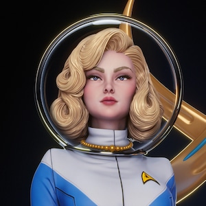 May include: A stylized figurine of a person with blonde hair styled in waves, wearing a white and blue uniform with a gold delta-shaped emblem on the chest. The figure is encased in a clear circular helmet and wears a gold beaded necklace.