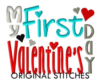 Op de afbeelding: Borduurwerk met de tekst "My First Valentine's Day" in verschillende kleuren. De tekst wordt omringd door kleine hartjes in rood, zwart en grijs.