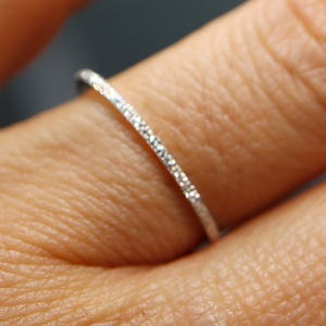 May include: A delicate silver ring with a thin band, encrusted with small, sparkling gemstones. The ring is shown on a person's finger, highlighting its fine details and elegant design. This piece of jewelry is perfect for everyday wear or special occasions.