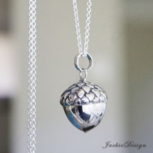 May include: A silver acorn pendant necklace. The pendant is a detailed, three-dimensional acorn with a textured cap and a smooth, rounded body. The necklace chain is delicate and silver, with a simple clasp.