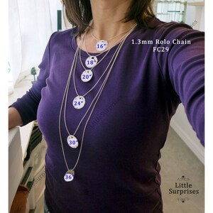May include: A woman wearing a purple shirt displays a set of silver necklaces with varying lengths. Each necklace features a round pendant and is labeled with its length in inches: 16", 18", 20", 24", 30", and 36". The text "1.3mm Rolo Chain FC29" is also visible.