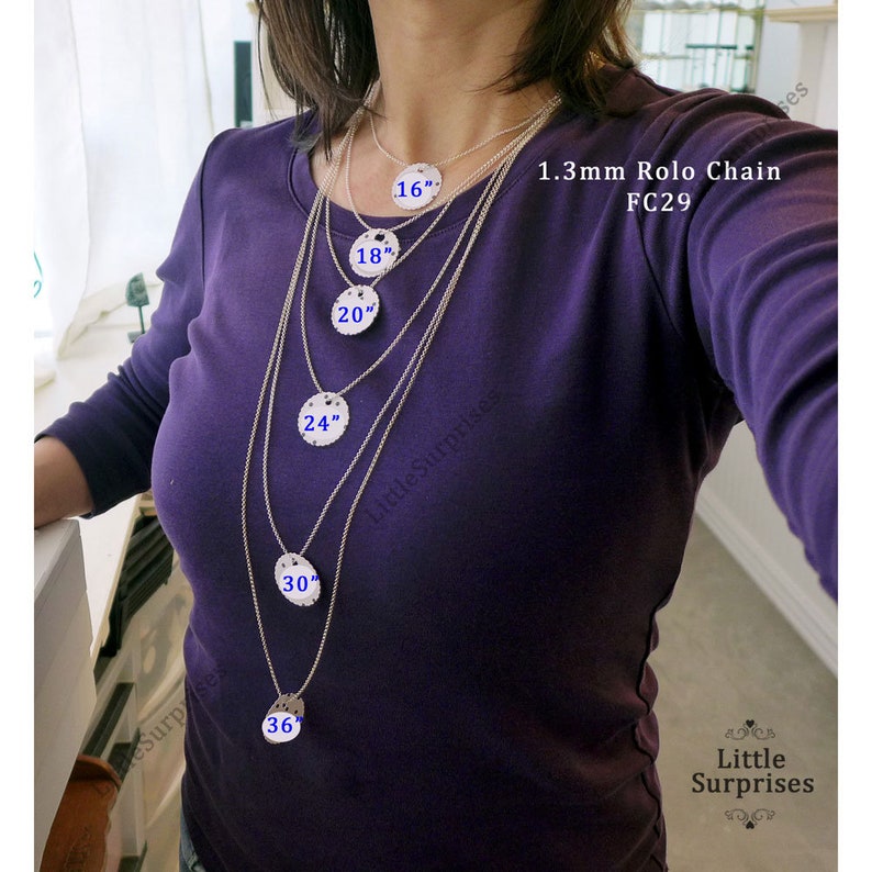 May include: A woman wearing a purple shirt displays a set of silver necklaces with varying lengths. Each necklace features a round pendant and is labeled with its length in inches: 16", 18", 20", 24", 30", and 36". The text "1.3mm Rolo Chain FC29" is also visible.