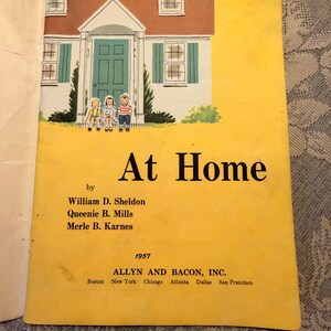 May include: A vintage 1957 book titled At Home by William D. Sheldon, Queenie B. Mills, and Merle B. Karnes, published by Allyn and Bacon, Inc. The cover features a yellow background with an illustration of a house and three children sitting.