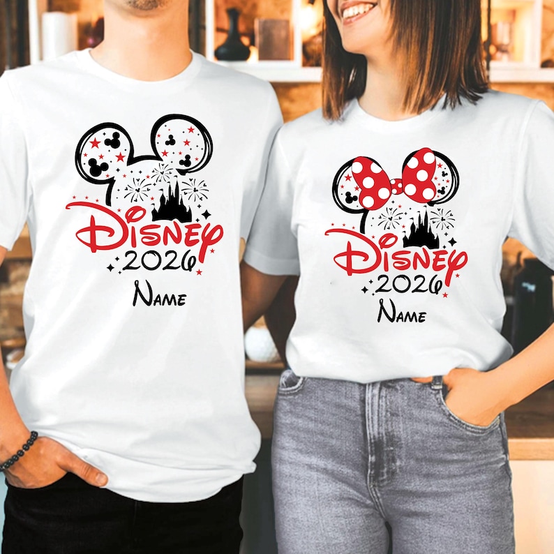 K&ouml;nnte beinhalten: Wei&szlig;e T-Shirts mit einem Disney-Motiv. Ein Shirt zeigt einen schwarzen Mickey Mouse-Kopf mit roten Sternen, Feuerwerk und dem Text "Disney 2026 Name" in Rot. Das andere Shirt hat eine rote Schleife mit Punkten.