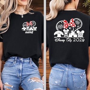 May include: Black t-shirt with a white graphic of a Minnie Mouse bow, fireworks, and a castle design. The front of the shirt has the word "NAME" and the back says "Disney Trip 2026".