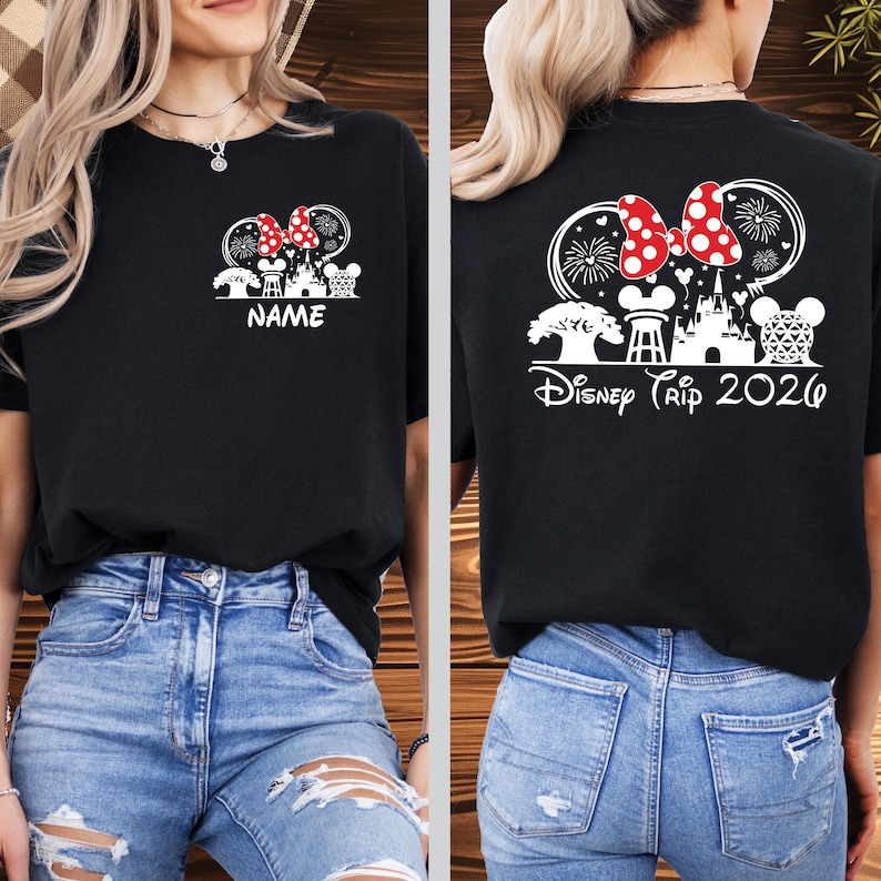 May include: Black t-shirt with a white graphic of a Minnie Mouse bow, fireworks, and a castle design. The front of the shirt has the word "NAME" and the back says "Disney Trip 2026".