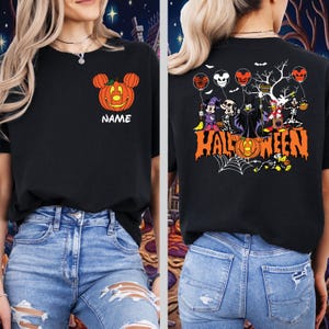Puede incluir: Una camiseta negra con un gráfico frontal de una calabaza naranja con orejas de ratón y el texto NAME. El gráfico trasero muestra varios personajes de dibujos animados con disfraces de Halloween, globos y el texto naranja HALLOWEEN.