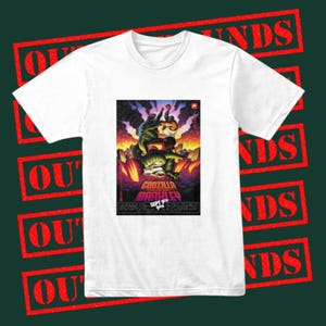 May include: White t-shirt featuring a colorful graphic of a monster battle scene with the text "Godzilla Brawley" and "Sept 9th". The design includes a green monster, a human figure, and a fiery background.