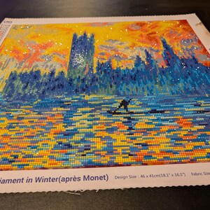 May include: Diamond painting of London Parliament in Winter, featuring a vibrant sunset and a silhouetted figure. The artwork, measuring 18.1 x 16.1 inches, uses a mosaic of colorful gems to depict the scene. The fabric size is 21.2 x 19.3 inches.