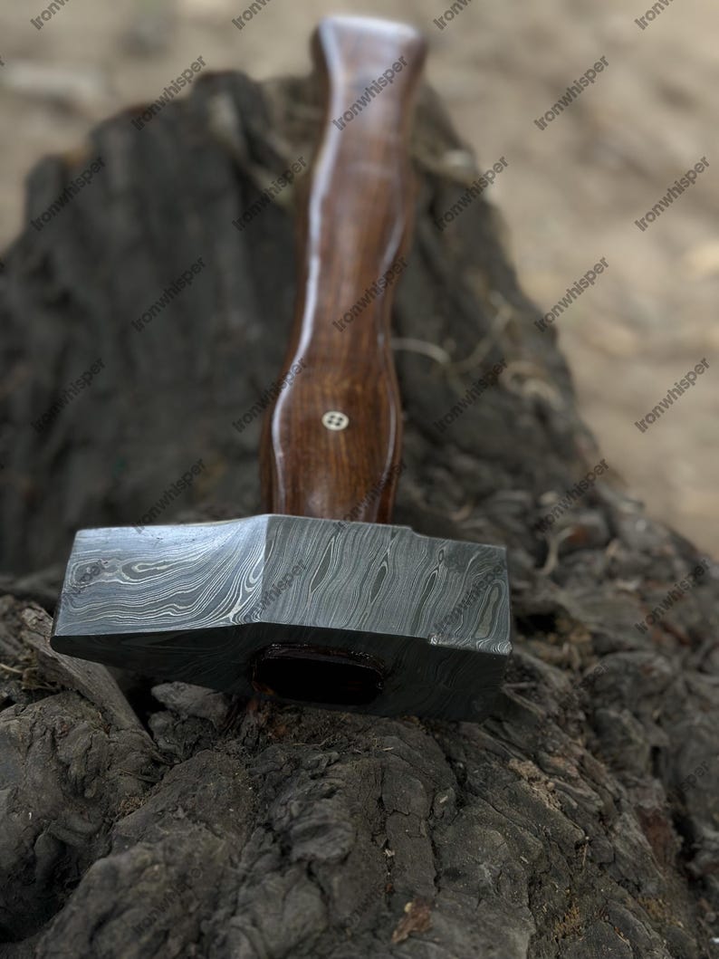May include: A handcrafted hammer with a dark wooden handle and a patterned steel head. The hammer's head is a dark gray color with a unique swirling pattern. The handle is a rich brown color. A tool for woodworking or metalworking.