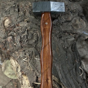 May include: A handcrafted hammer with a patterned steel head and a polished wooden handle. The handle is a rich brown color and features a decorative inlay. The hammer is designed for woodworking or metalworking.