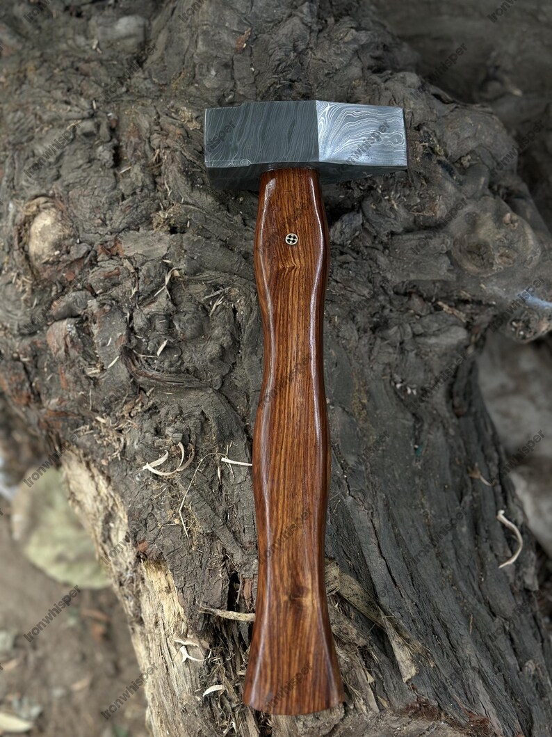 May include: A handcrafted hammer with a patterned steel head and a polished wooden handle. The handle is a rich brown color and features a decorative inlay. The hammer is designed for woodworking or metalworking.