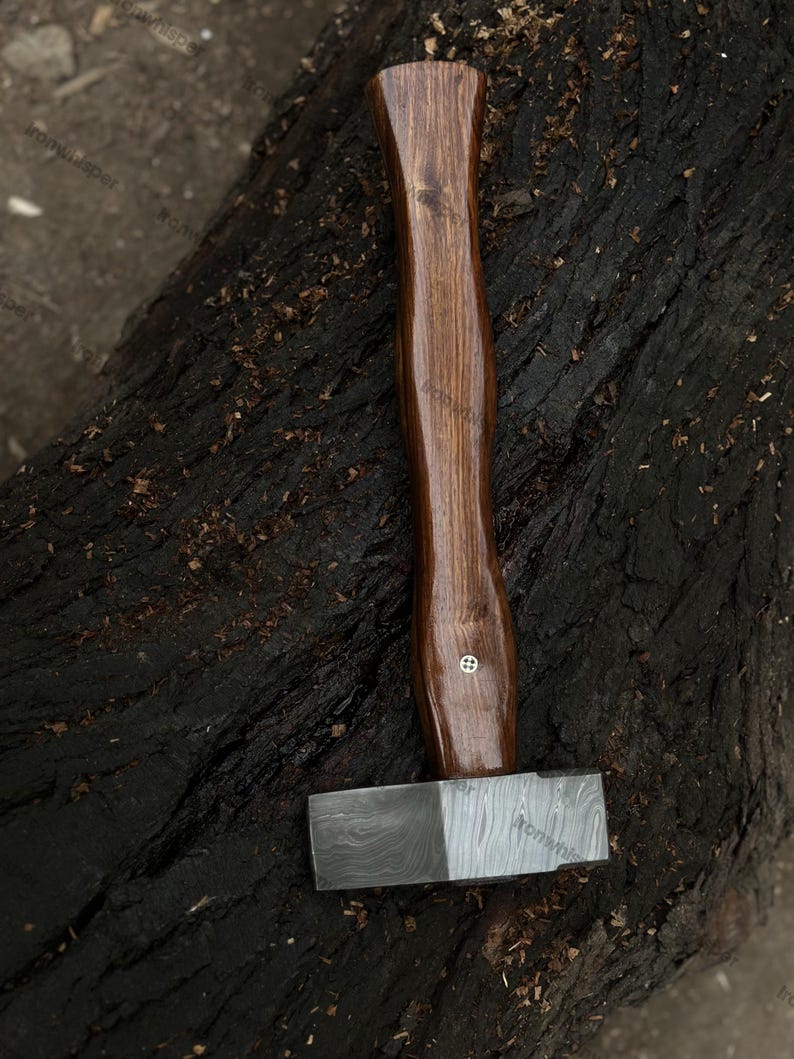 May include: A handcrafted hammer with a dark wooden handle and a patterned steel head. The handle is a rich brown color, and the head has a contrasting silver and dark gray pattern. The hammer is designed for woodworking or metalworking.