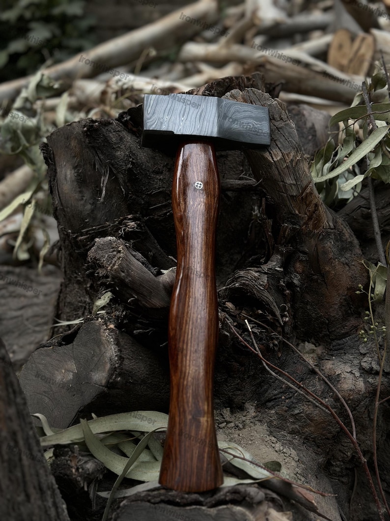 May include: A handcrafted hammer with a dark, patterned steel head and a polished, dark wood handle. The handle features a decorative metal inlay. The hammer is designed for woodworking and metalworking.