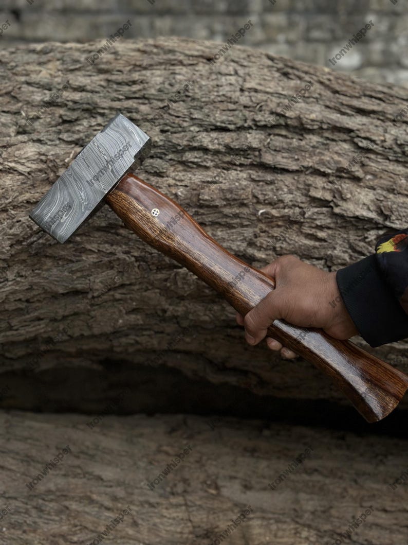 May include: A handcrafted hammer with a patterned steel head and a dark wooden handle. The handle has a smooth, polished finish and a decorative inlay. The hammer is held against a textured, natural wood background.