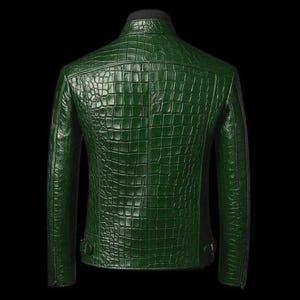 May include: A dark green leather jacket with a textured, crocodile-skin pattern. The jacket has a stand-up collar, long sleeves, and a zipper closure. The back of the jacket is visible, showcasing the detailed pattern and design.